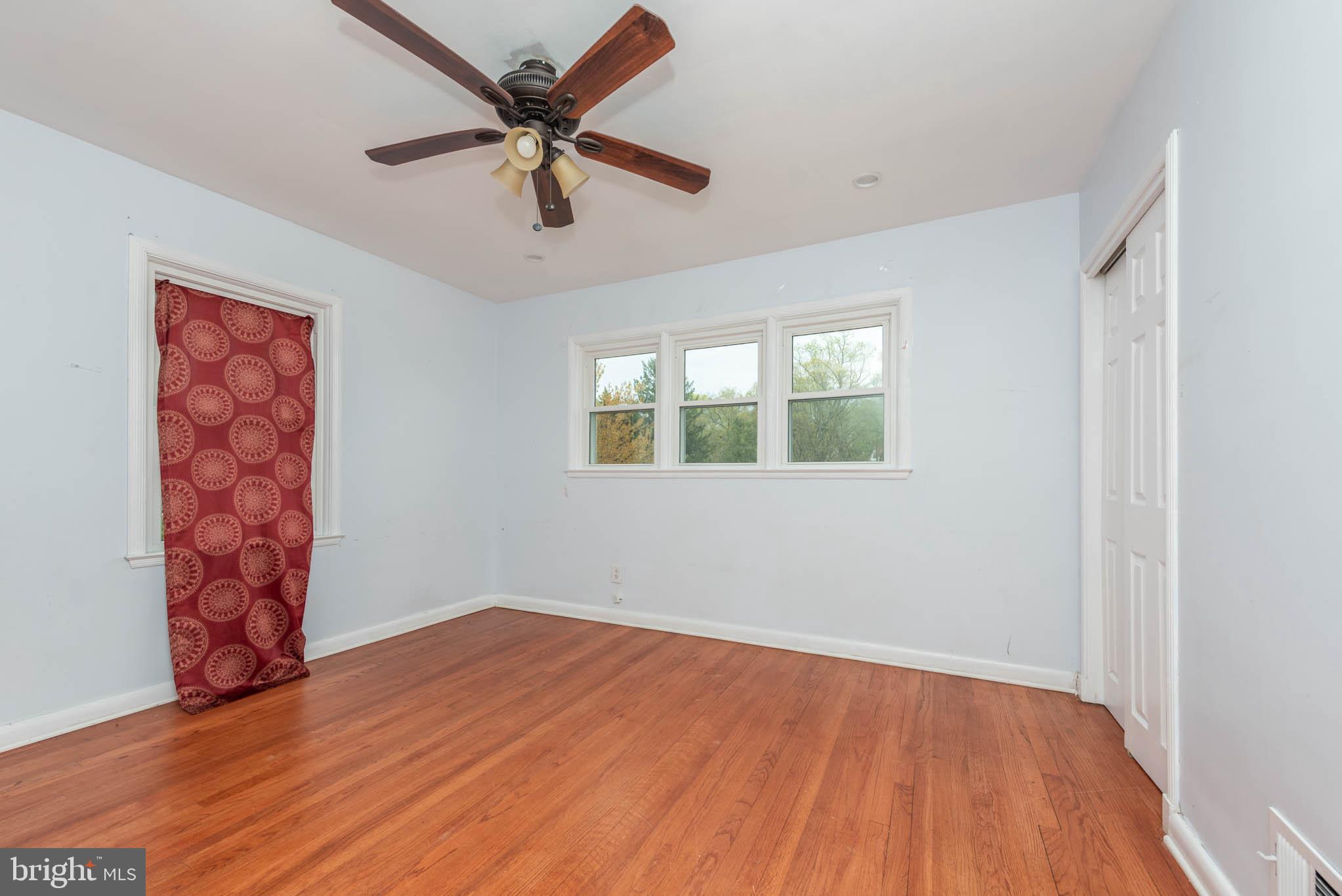 6702 Queens Ferry Road Baltimore, MD 21239 - Photo 11 of 40 an empty room with wooden floor chandelier fan and windows