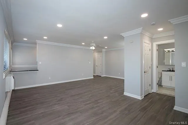 a view of an empty room with wooden floor and a kitchen