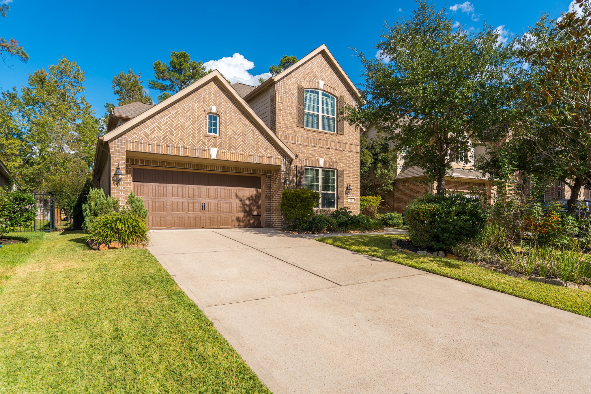 30 Fury Ranch Place The Woodlands, TX 77375 - Photo 7 of 47 This photo shows a charming brick two-story home with a well-maintained front yard and a spacious driveway leading to a two-car garage. The house features a classic design with large windows and is surrounded by mature trees, offering a welcoming and serene atmosphere.