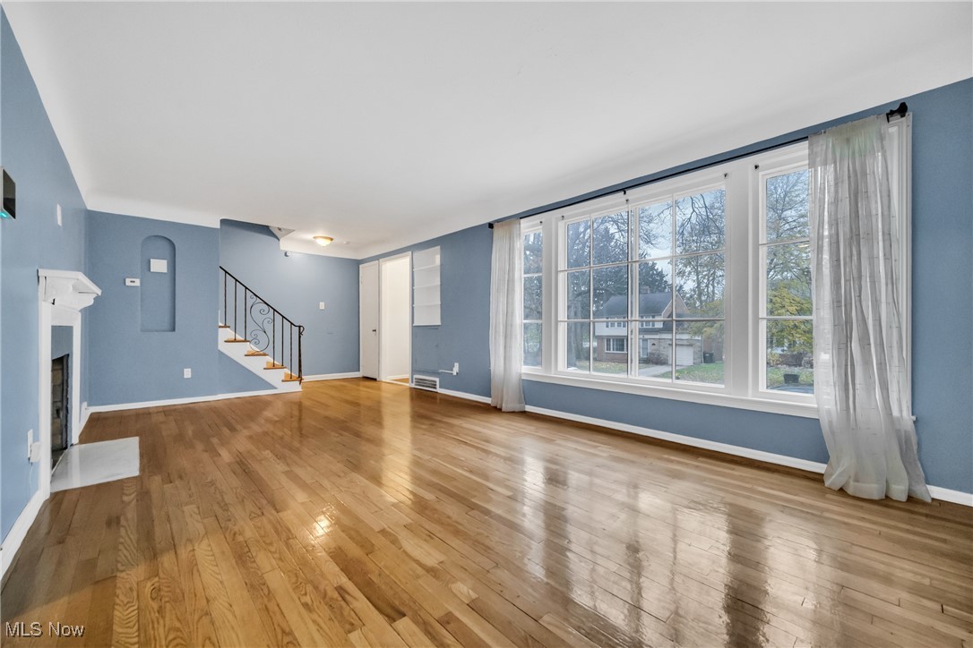 1605 Laclede Road Cleveland, OH 44121 - Photo 14 of 40 Unfurnished living room with a fireplace with flush hearth, stairway, hardwood / wood-style floors, and plenty of natural light