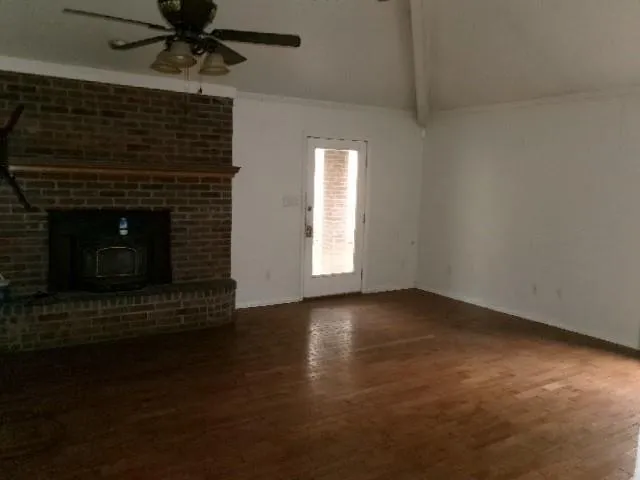 a view of an empty room with wooden floor a fireplace and a window