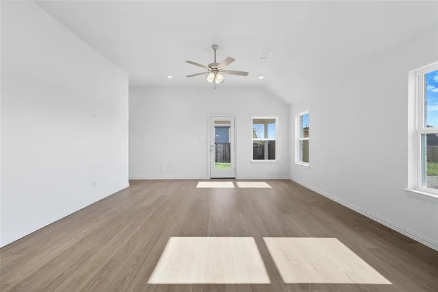 an empty room with wooden floor ceiling fan and windows