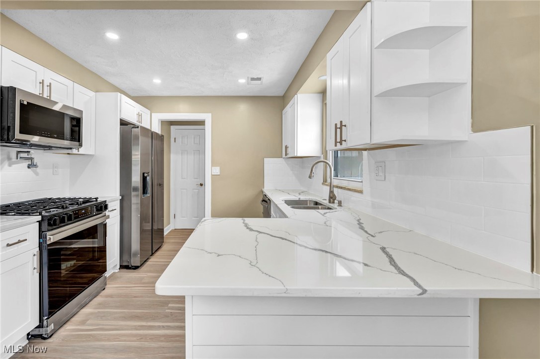 1447 East Sprague Road Independence, OH 44131 - Photo 9 of 47 Kitchen with sink, white cabinetry, light stone counters, light wood-type flooring, and appliances with stainless steel finishes