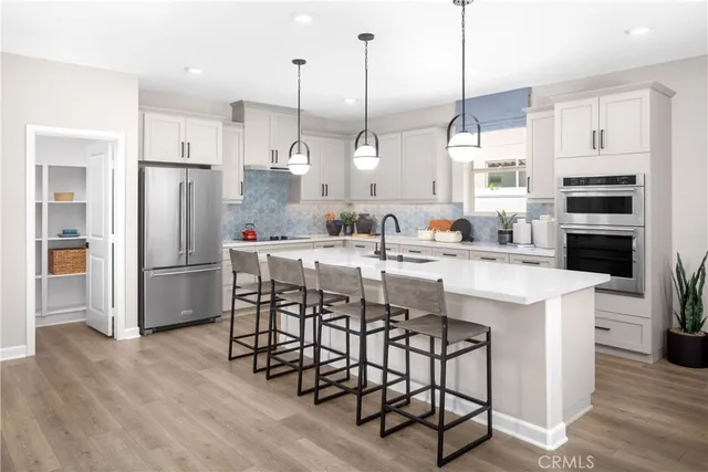 a kitchen with stainless steel appliances kitchen island granite countertop a refrigerator a stove a sink and white cabinets with wooden floor