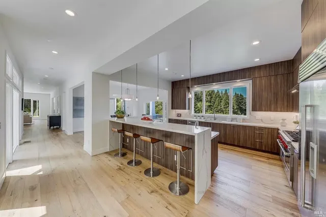 a kitchen with stainless steel appliances granite countertop a refrigerator a sink dishwasher a dining table and chairs with wooden floor