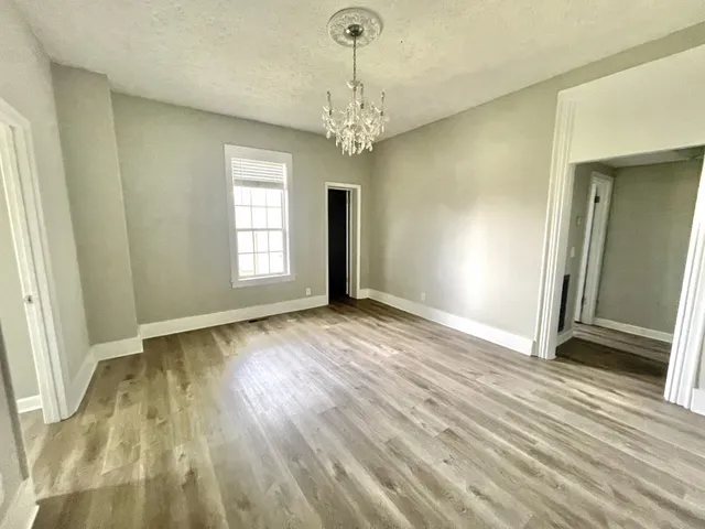 an empty room with wooden floor chandelier and windows