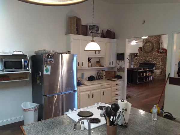 a kitchen with stainless steel appliances kitchen island granite countertop a refrigerator a stove a sink a dining table and chairs with wooden floor