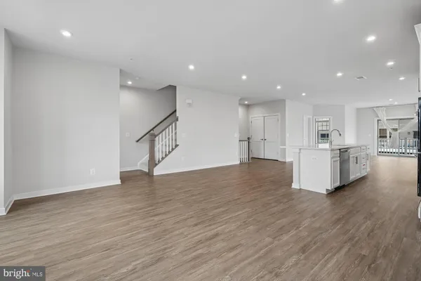 a view of an empty room with wooden floor and a kitchen