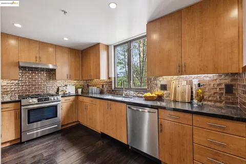 a kitchen with stainless steel appliances granite countertop a refrigerator a stove and a sink with wooden floor