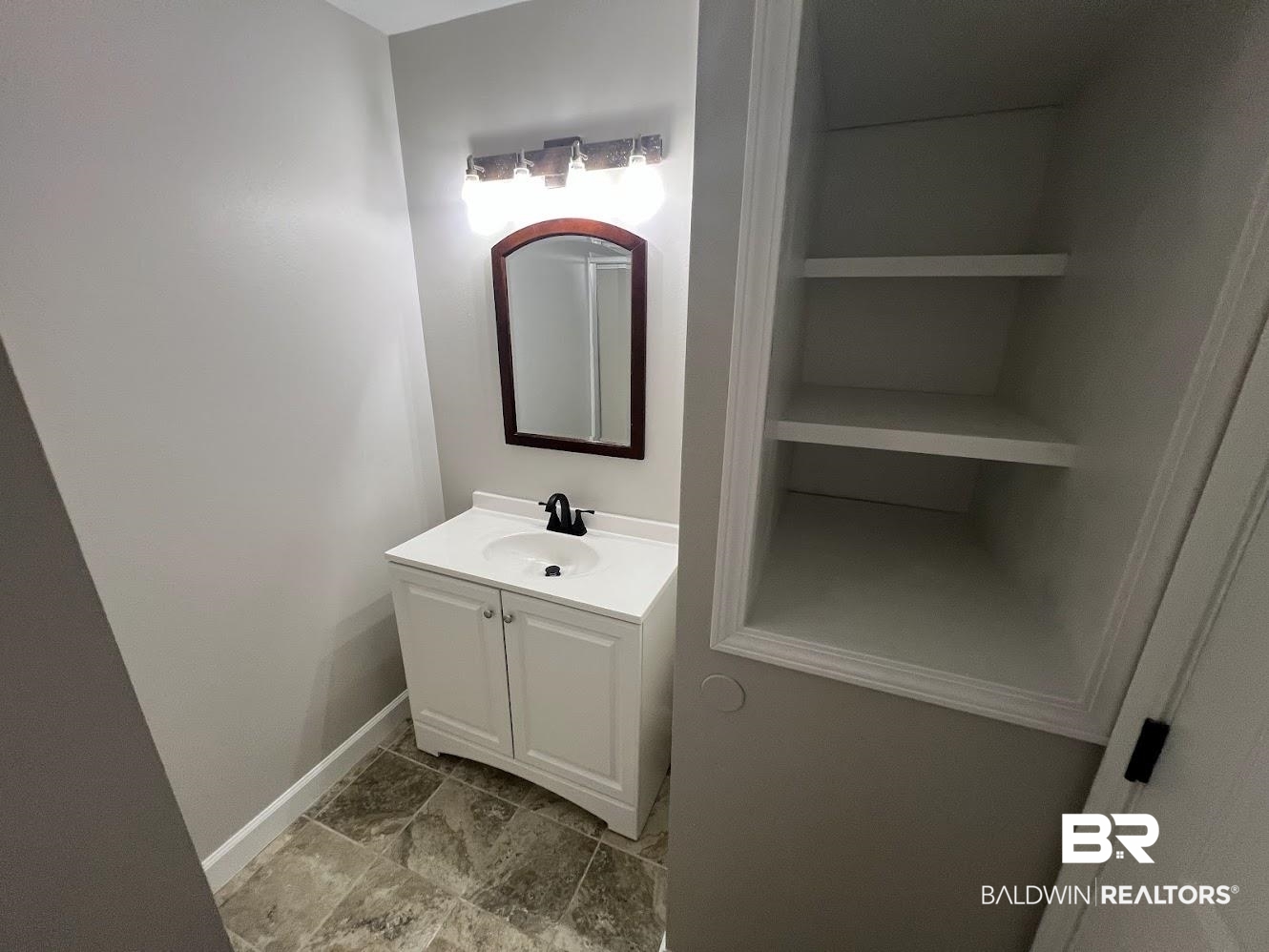 266 Ridgewood Drive Daphne, AL 36526 - Photo 23 of 34 Modern vanity with a white countertop and integrated sink, complemented by a dark framed mirror and a three-light fixture