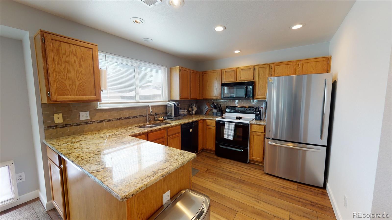 10482 Hyacinth Street Highlands Ranch, CO 80129 - Photo 16 of 40 a kitchen with granite countertop a refrigerator oven a sink dishwasher and wooden cabinets with wooden floor