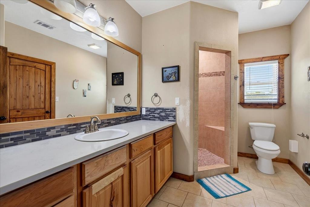 11591 Farm To Market 59 Athens, TX 75751 - Photo 19 of 40 2nd Primary Bathroom on level 1 featuring an oak vanity with light quartz countertop and undermount sink, backsplash, big mirror, cabinets and drawers. Large oversize walk-in shower with pebble stone, oversize walk-in closet, tile floor