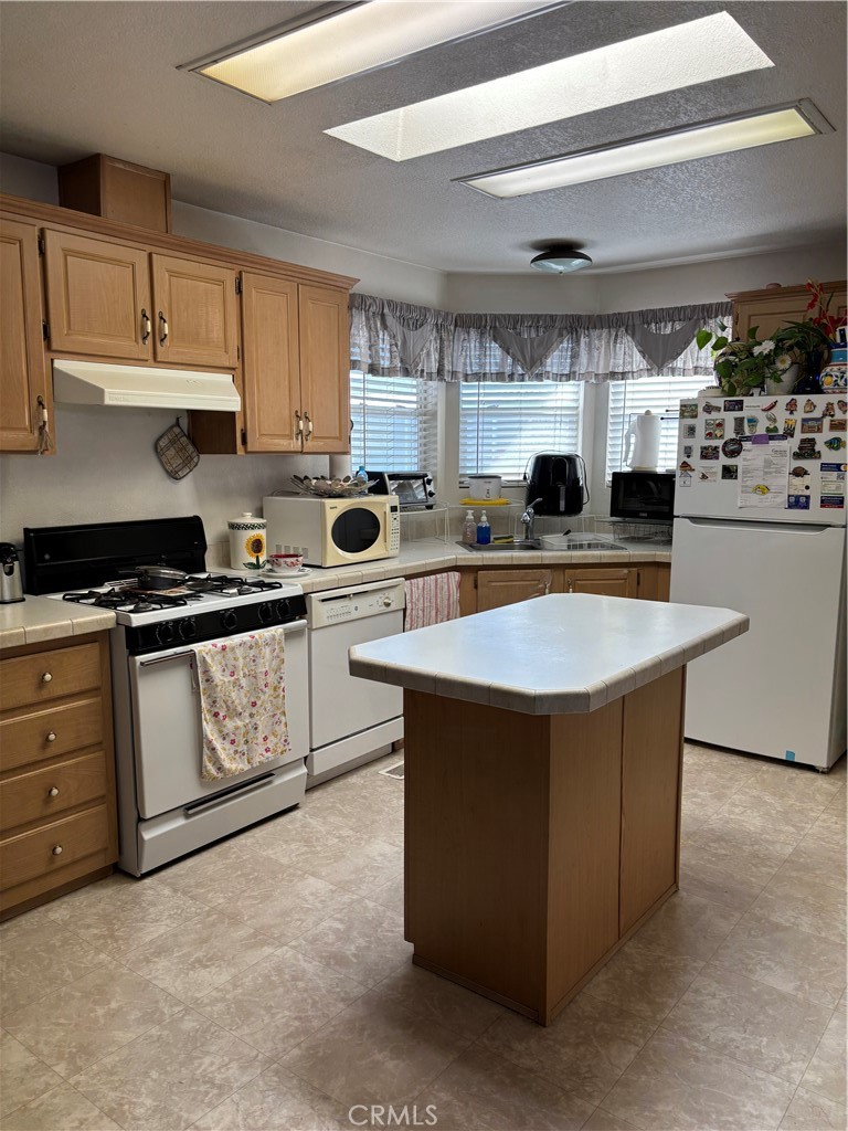8389 Baker Avenue, Unit 82 Rancho Cucamonga, CA 91730 - Photo 4 of 13 a kitchen with kitchen island granite countertop a stove top oven a sink dishwasher and white cabinets with wooden floor