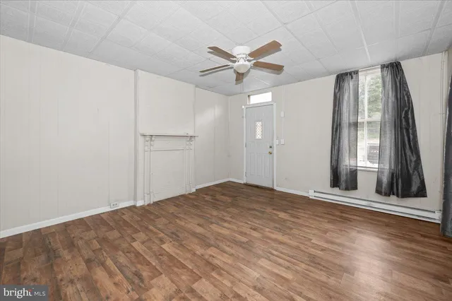 a view of an empty room with wooden floor and a ceiling fan