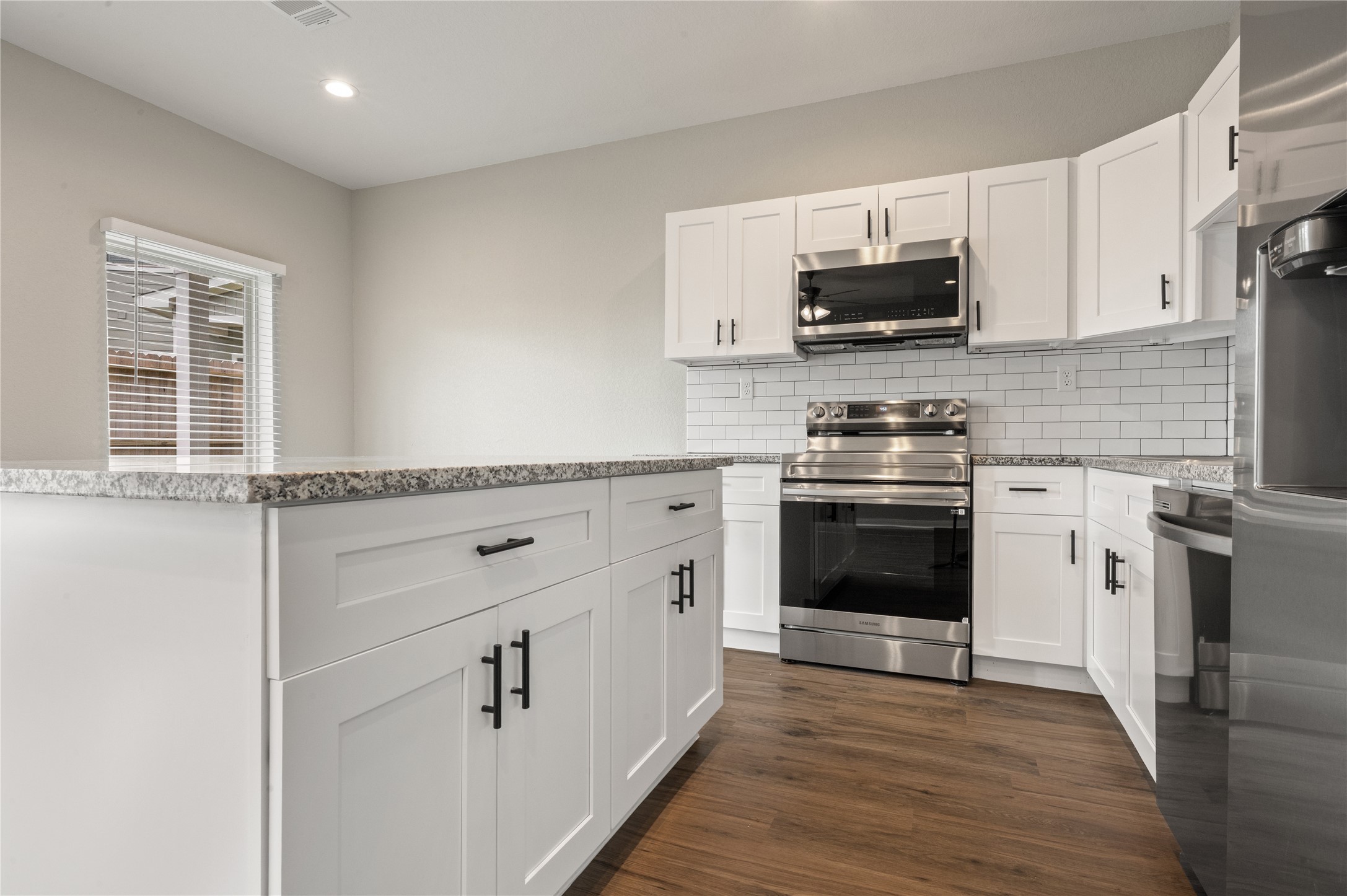 14010 Longstreet Road, Unit 2 Willis, TX 77318 - Photo 21 of 29 Modern kitchen with white cabinetry, stainless steel appliances, granite countertops, and subway tile backsplash. Features wood flooring and ample natural light.