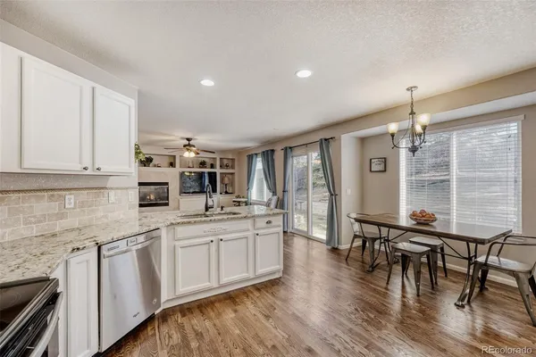 a kitchen with stainless steel appliances granite countertop a stove top oven a sink a dining table and chairs with wooden floor