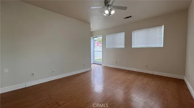 an empty room with wooden floor chandelier fan and windows