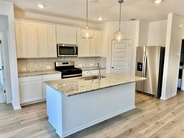 a kitchen with stainless steel appliances granite countertop a refrigerator a stove a sink and a microwave with wooden floor