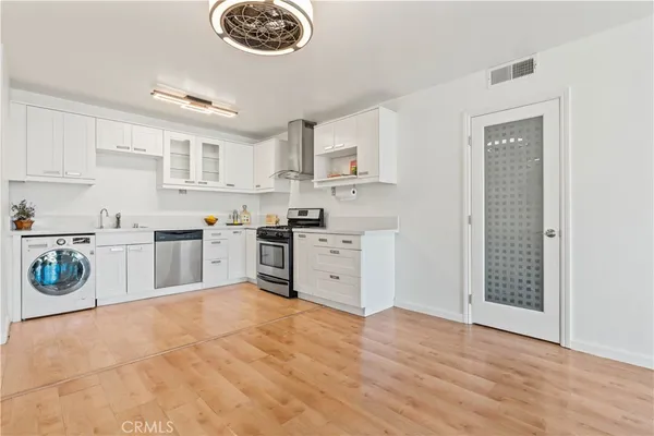 a kitchen with stainless steel appliances granite countertop a stove top oven a sink dishwasher and white cabinets with wooden floor