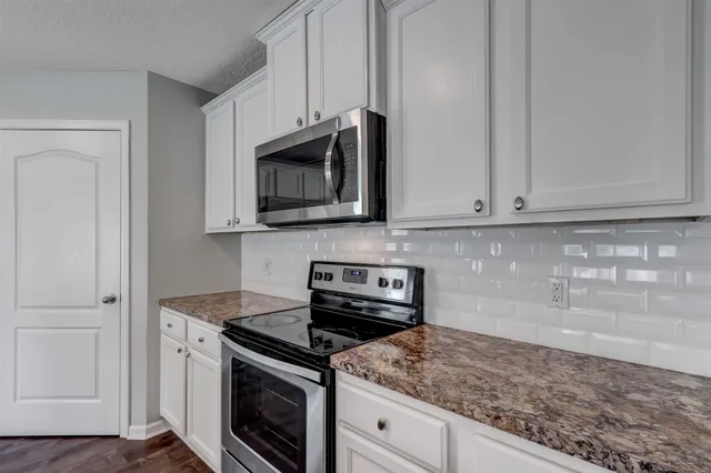 a kitchen with stainless steel appliances granite countertop white cabinets granite counter tops and a wooden floor