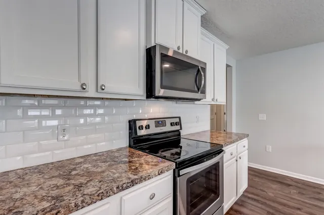a kitchen with granite countertop a stove top oven microwave and cabinets
