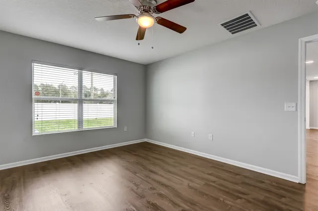 an empty room with wooden floor fan and windows