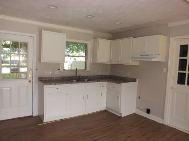 a kitchen with granite countertop white cabinets white appliances wooden floor and a window