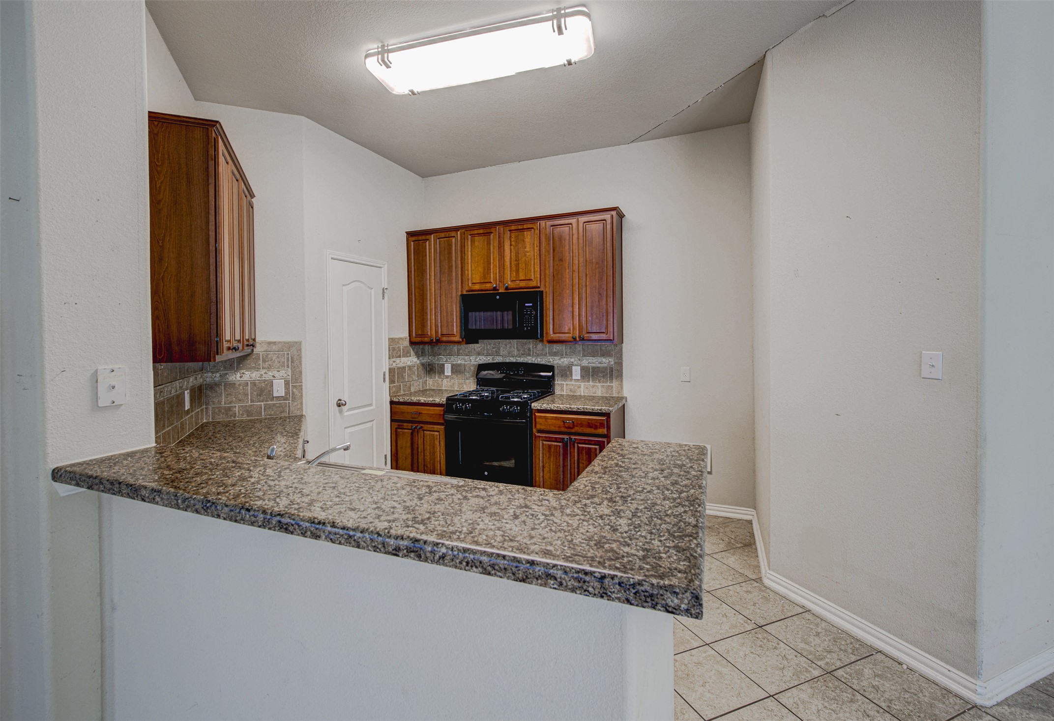 2090 Intrepid Drive Buda, TX 78610 - Photo 8 of 24 Kitchen with black appliances, a peninsula, tasteful backsplash, light tile patterned floors, and wood finish cabinetry
