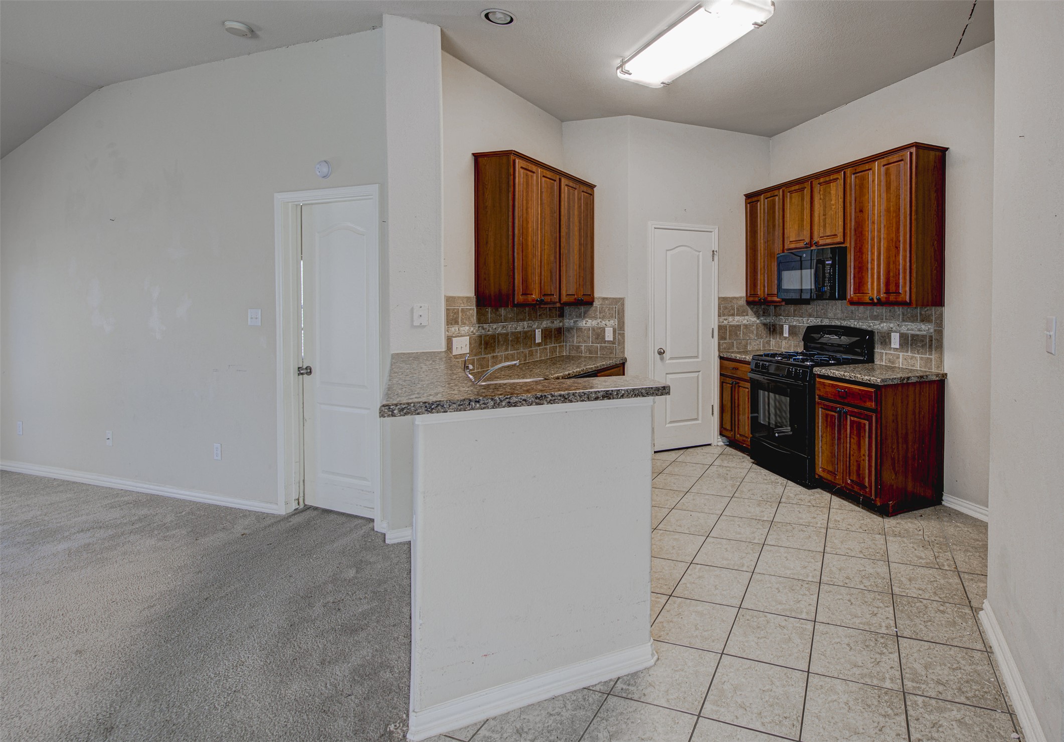 2090 Intrepid Drive Buda, TX 78610 - Photo 9 of 24 Kitchen featuring black appliances, a peninsula, light tile patterned floors, decorative backsplash, and vaulted ceiling