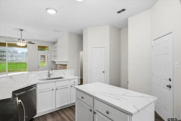 a kitchen with a sink dishwasher and white cabinets with wooden floor