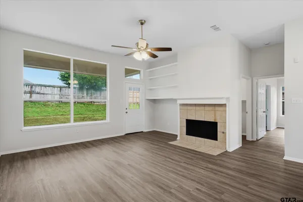 an empty room with wooden floor fireplace and windows