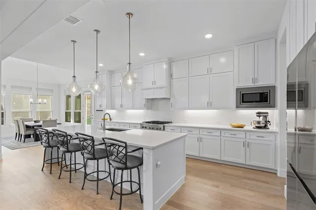 a kitchen with stainless steel appliances granite countertop a stove a sink a oven a dining table and chairs with white cabinets