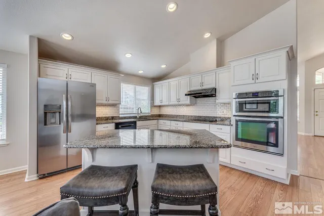 a kitchen with stainless steel appliances granite countertop a stove a sink a microwave a refrigerator and chairs