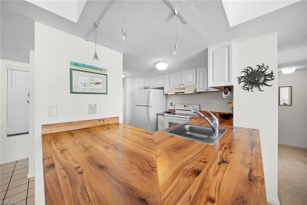 26300 Hickory Boulevard, Unit 503 Bonita Springs, FL 34134 - Photo 17 of 50 Kitchen with white appliances, hanging light fixtures, butcher block counters, white cabinetry, and under cabinet range hood