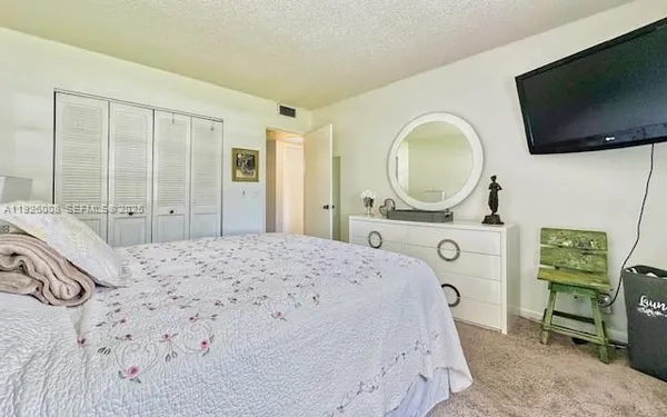 a bedroom with a bed a flat tv screen and a dresser