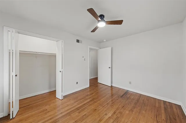 an empty room with wooden floor ceiling fan and windows