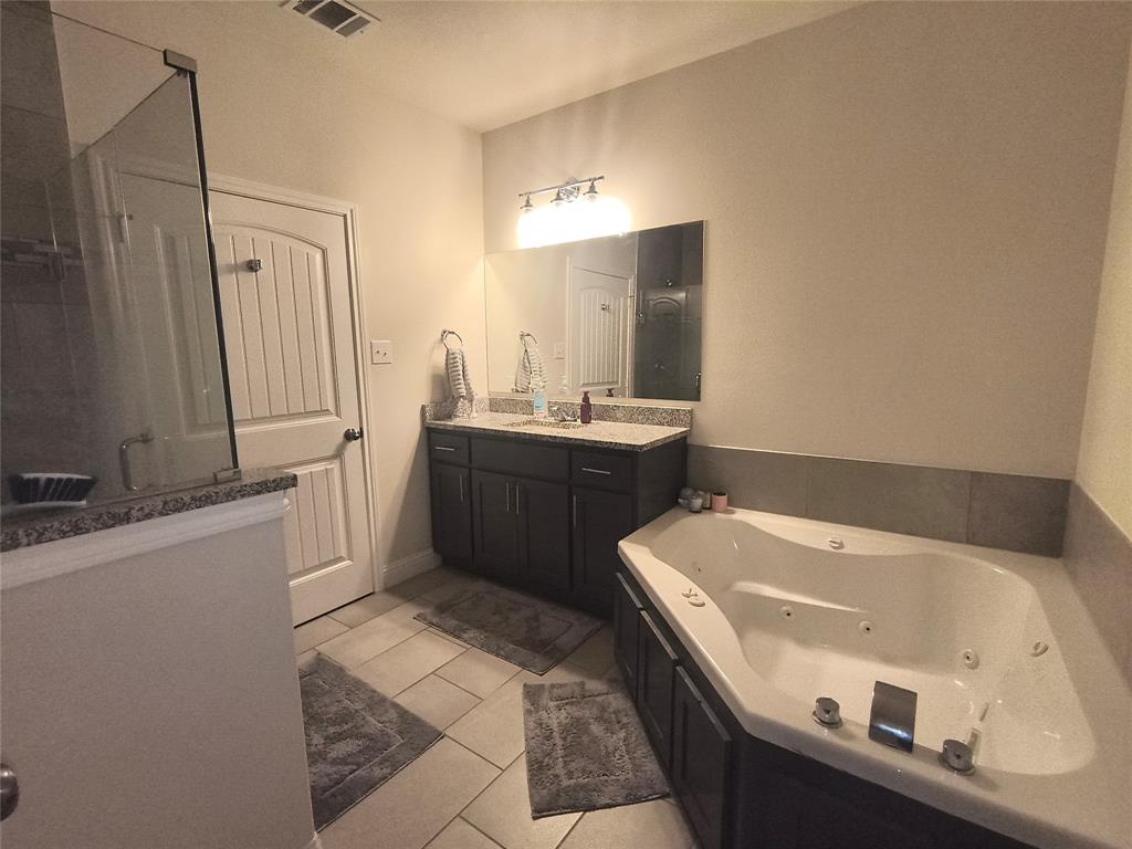 3027 Ames Road Lancaster, TX 75134 - Photo 23 of 35 Bathroom featuring a corner jetted soaking tub, a dark wood-finish vanity with a light-toned countertop, a frameless mirror, and a glass-enclosed shower