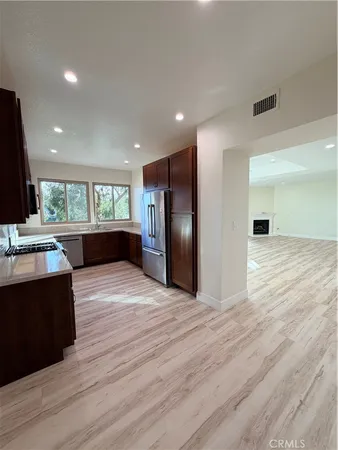 a view of an empty room with wooden floor and a kitchen