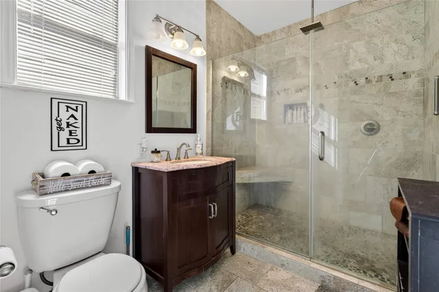 a bathroom with a toilet sink vanity granite and shower