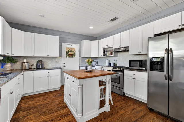 a kitchen with stainless steel appliances granite countertop a stove a sink dishwasher a refrigerator and white cabinets with wooden floor