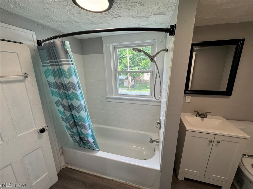 674-676 Carlysle Street Akron, OH 44310 - Photo 17 of 20 Second floor bathroom featuring a white vanity with integrated sink, a rectangular framed mirror, a bathtub with white tile surround, and wood-finish flooring