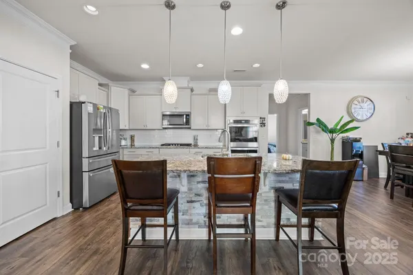 a kitchen with stainless steel appliances granite countertop a dining table chairs refrigerator and microwave