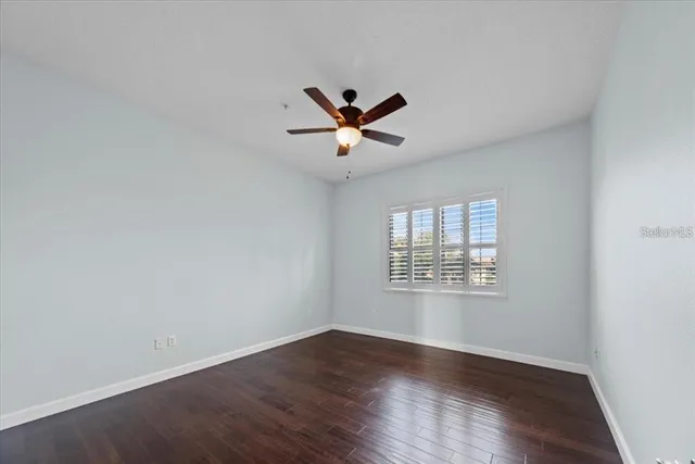 an empty room with wooden floor ceiling fan and windows