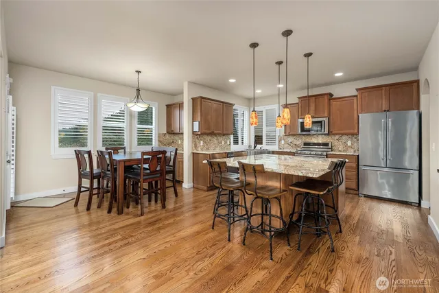 a kitchen with stainless steel appliances granite countertop a dining table chairs refrigerator and sink