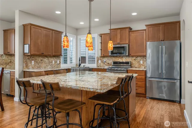 a kitchen with stainless steel appliances granite countertop a stove a refrigerator a kitchen island a dining table and chairs