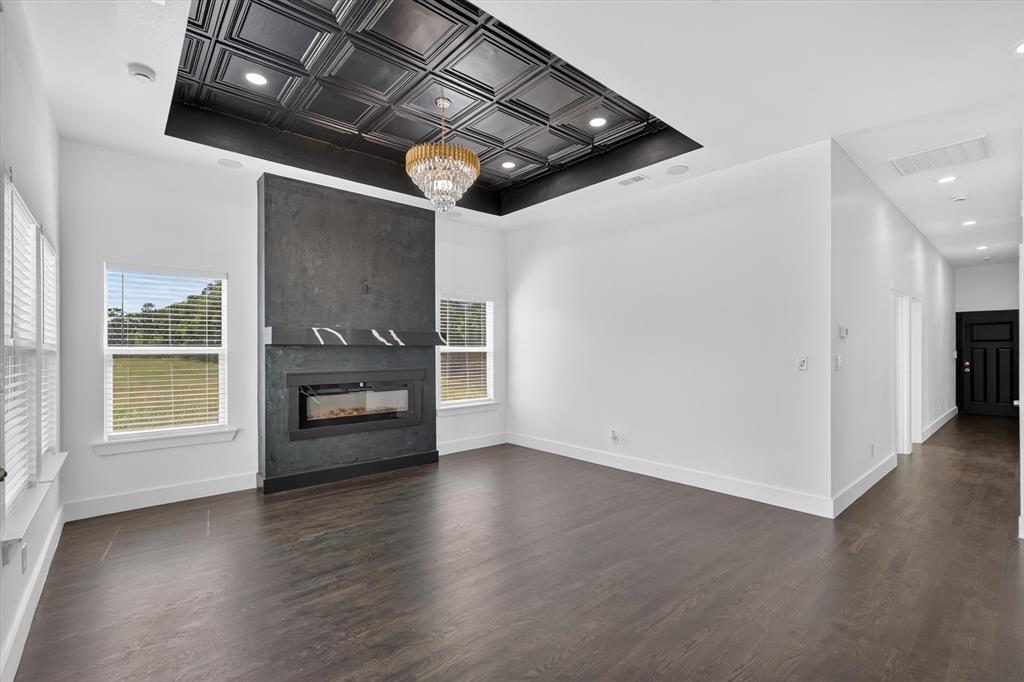 102 Shadywood Road Trinidad, TX 75163 - Photo 5 of 24 Spacious living area featuring a modern fireplace with a dark surround, a coffered ceiling with recessed lighting, an elegant chandelier, and wood-finish flooring