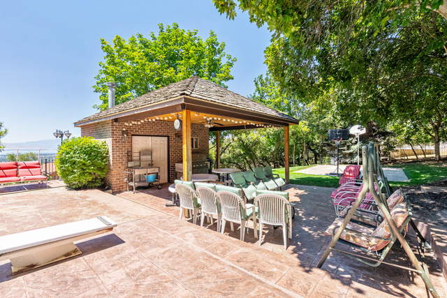 4093 North Imperial Way Provo, UT 84604 - Photo 82 of 96 Expansive stamped concrete patio featuring a brick-built outdoor kitchen structure with a covered dining area, string lighting, and mature landscaping