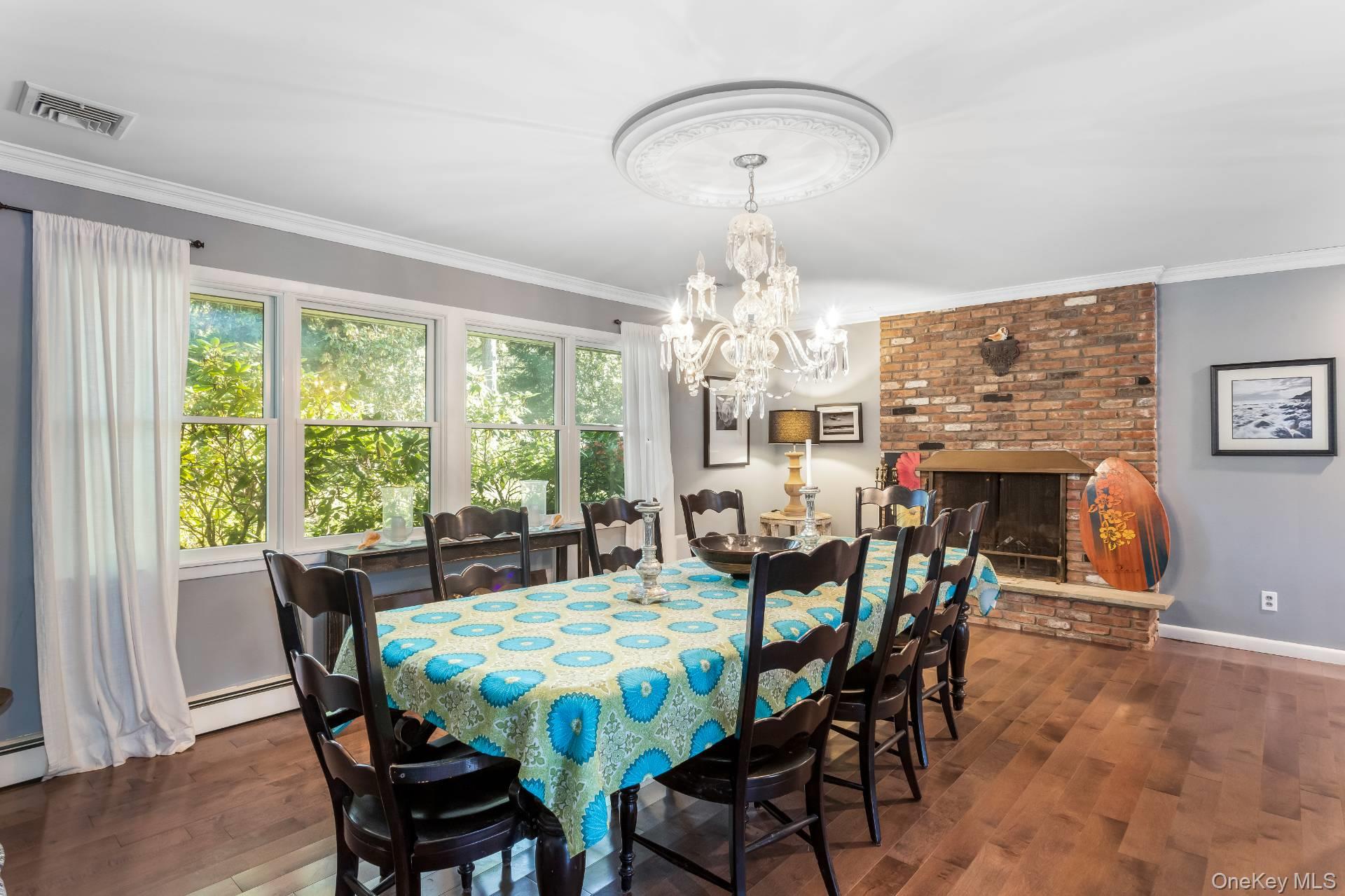 3693 Pine Neck Road Southold, NY 11971 - Photo 8 of 16 Dining room with dark wood finished floors, a brick fireplace, ornamental molding, a chandelier, and a baseboard radiator