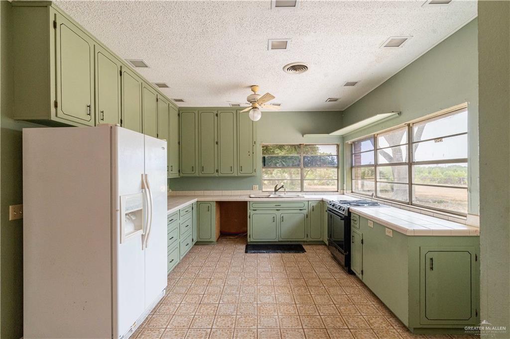 2351 Liberty Street Mercedes, TX 78570 - Photo 3 of 13 Kitchen featuring white refrigerator with ice dispenser, electric range, sink, green cabinets, and ceiling fan
