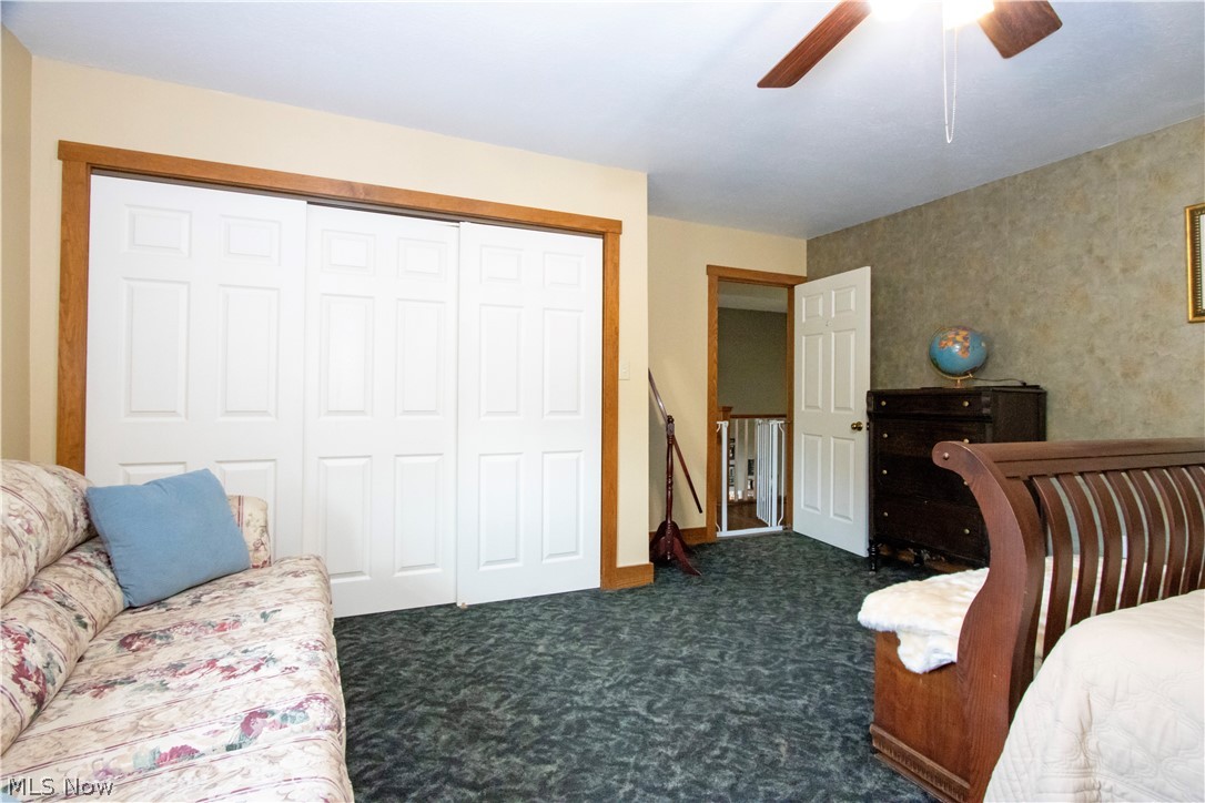 1043 North Honeytown Road Wooster, OH 44691 - Photo 16 of 46 Bedroom featuring three sliding closet doors with wood trim, textured accent wall, and a ceiling fan